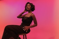 a woman in a black dress sitting on a stool