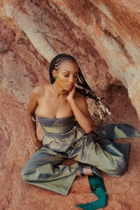 a woman in a green jumpsuit sitting on a rock