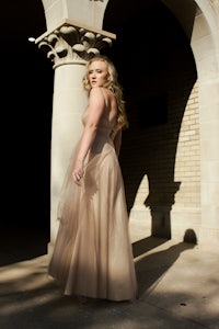 a woman in a long dress is posing in front of an archway