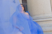 a woman in a blue tulle dress leaning against pillars