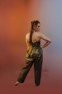 a woman in a green jumpsuit posing in front of an orange background