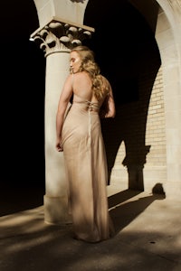 a woman in a long dress standing in front of pillars