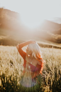 a woman sitting in a field at sunset