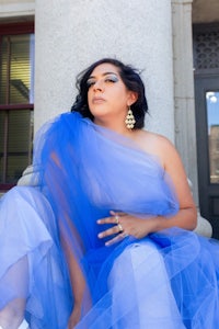 a woman in a blue tulle dress sits on the steps of a building