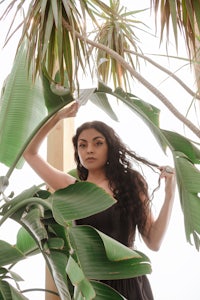 a woman in a black dress posing in front of a banana plant